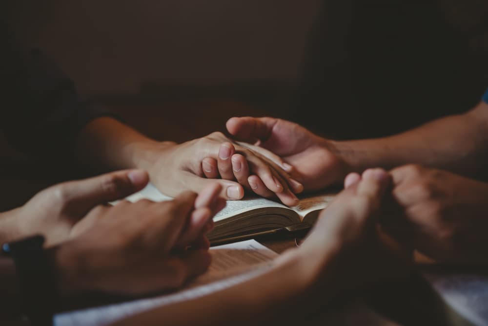 Holding hands praying over Bibles