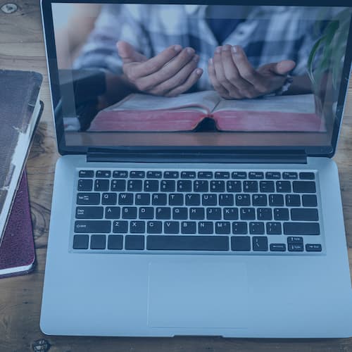Person praying in front of laptop with Bible