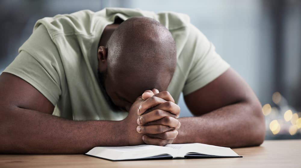 Man leaning over praying over open Bible